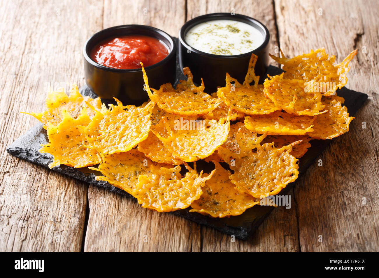 Golden organico formaggio cheddar chip con erbe aromatiche con salse close-up su una scheda su una tavola orizzontale. Foto Stock