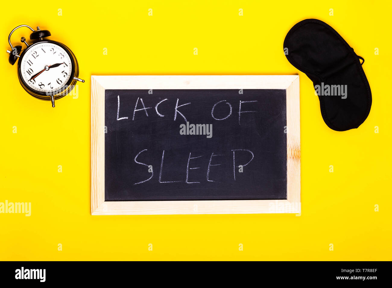 Concetto di sonno che mostra una sveglia e la maschera per gli occhi con un bordo nero la lettura di mancanza di sonno in un backgroun giallo Foto Stock