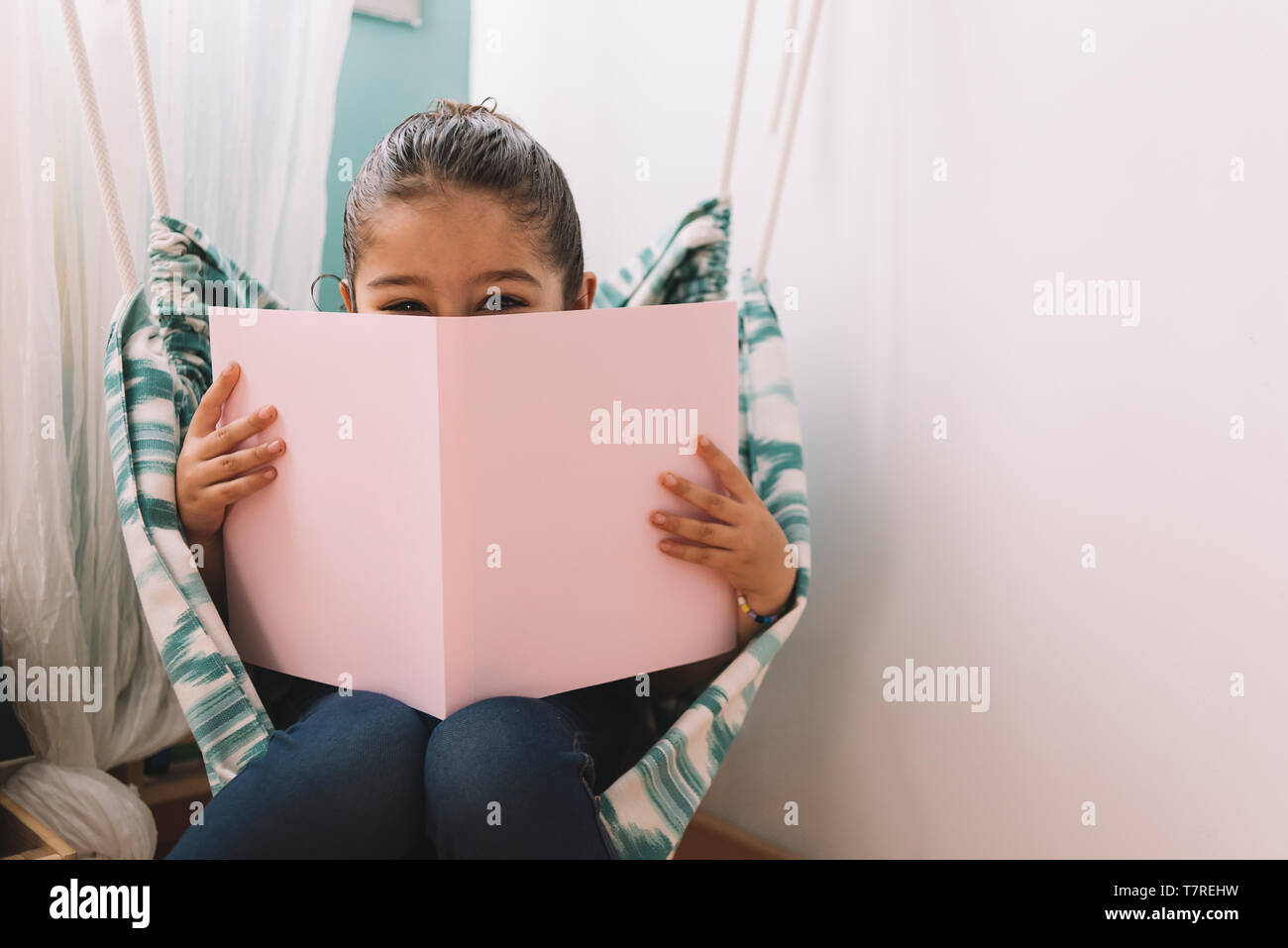 Dolce felice bambina leggendo un libro nella sua camera da letto vicino alla finestra, funny bel bambino divertirsi nella camera dei ragazzi, copia spazio per il testo Foto Stock