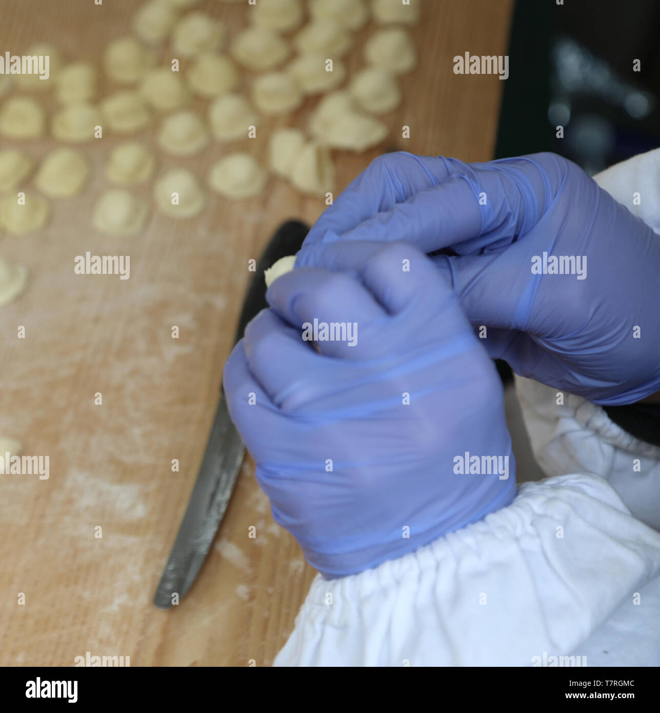 Le mani con guanti blu durante la produzione italiana di cibo fresco chiamato Orecchiette un piatto tipico della regione Puglia in Italia Meridionale Foto Stock