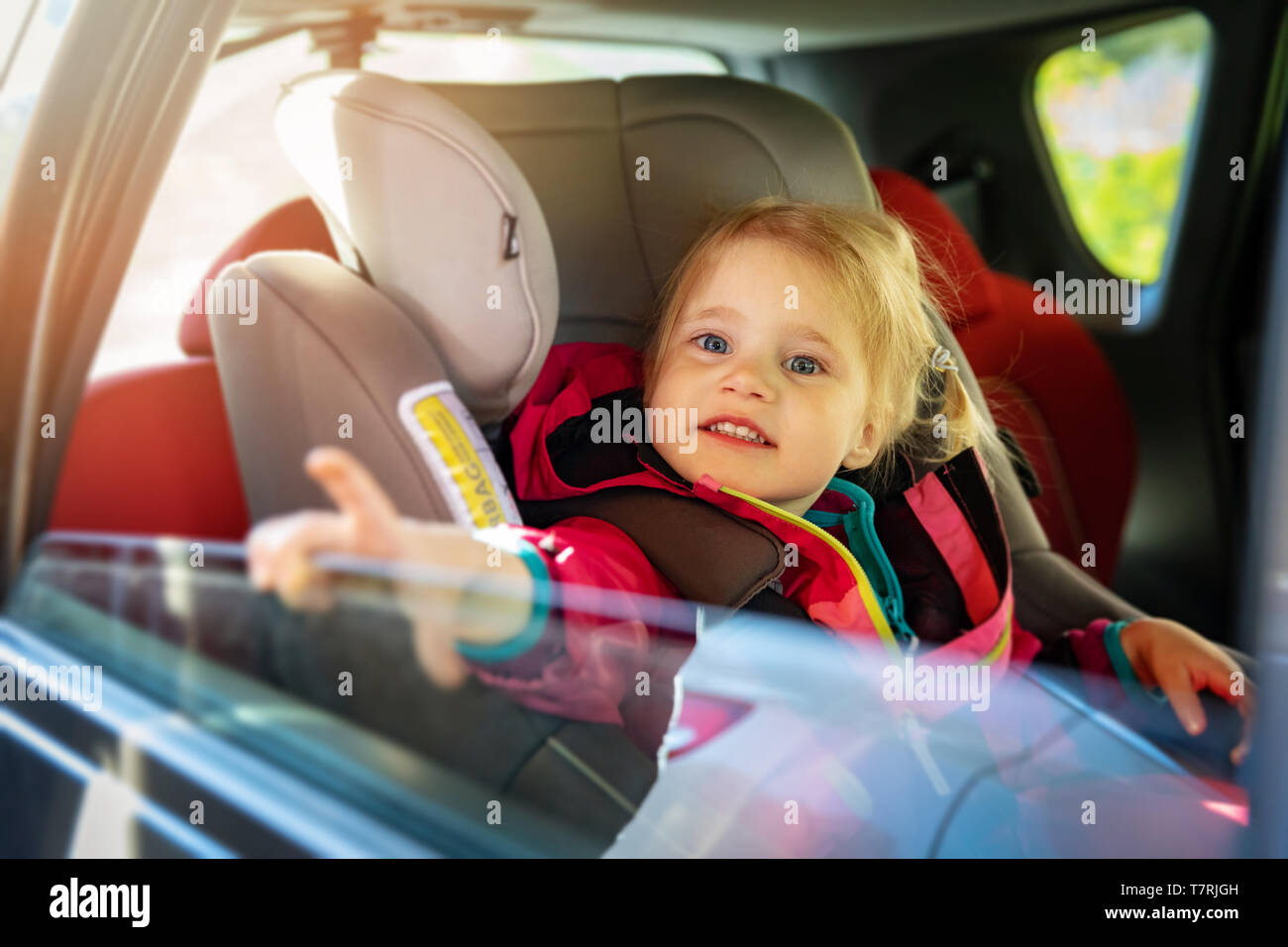 Poco sorridente ragazza seduta in un seggiolino da bambino per auto Foto Stock