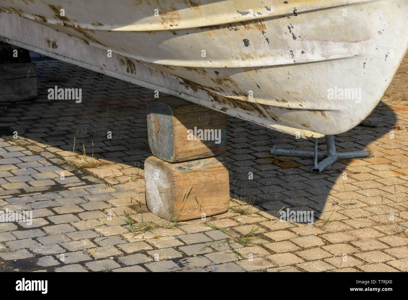 Piccola barca puntellato su un grande blocco di legno in un cantiere Foto Stock