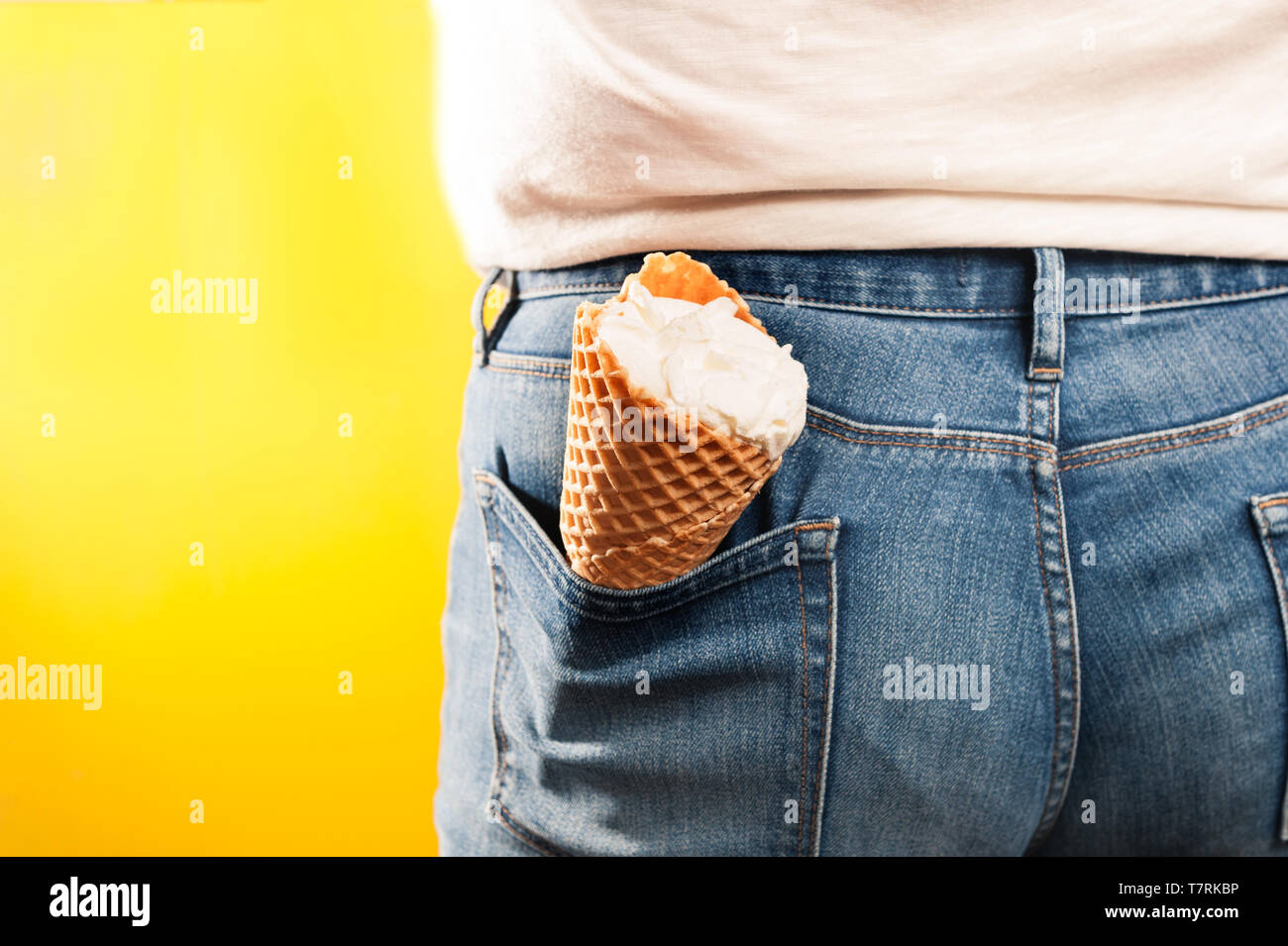 Cono gelato nella tasca dei jeans su sfondo giallo Foto Stock