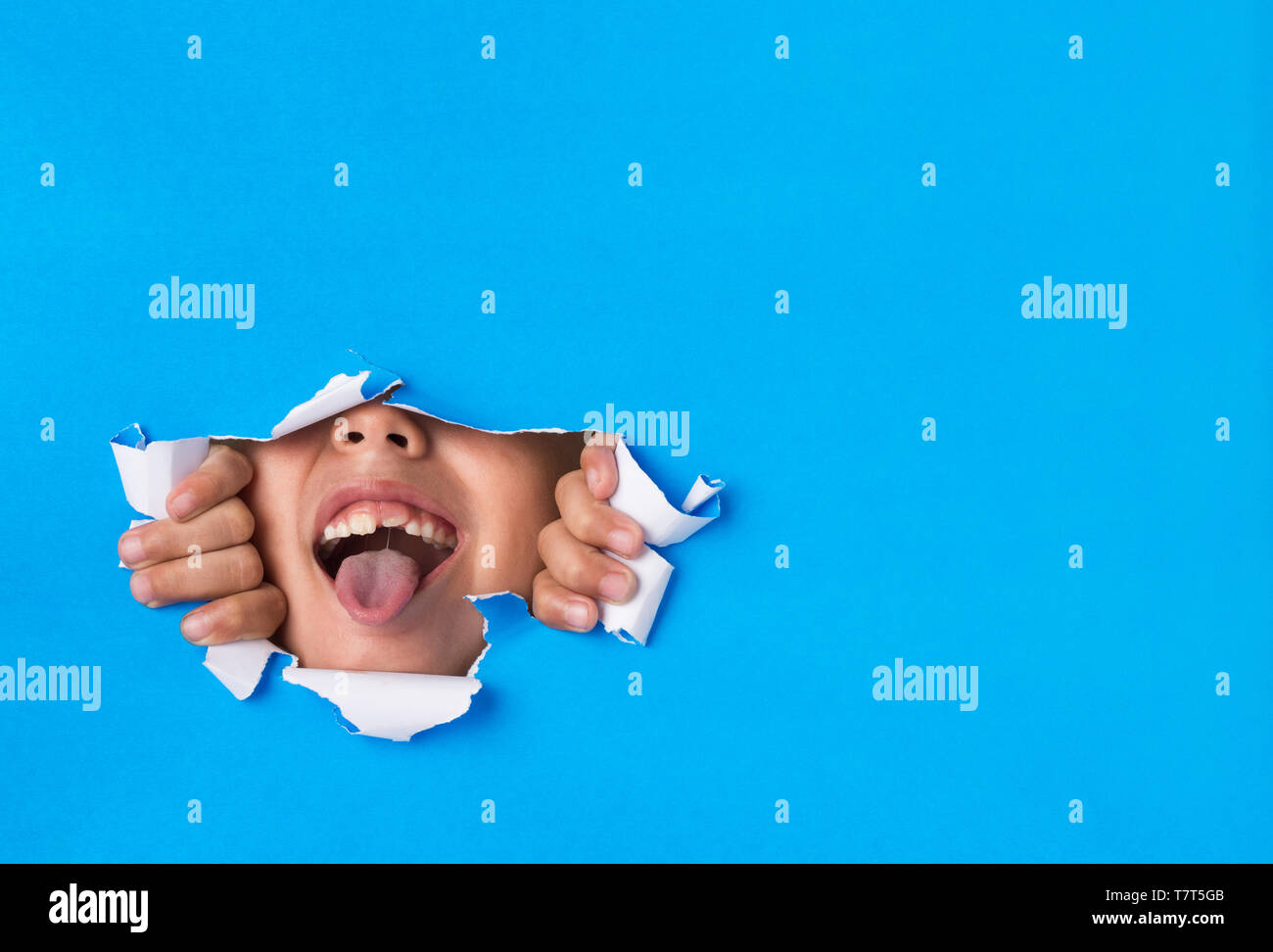 Ragazzo giovane prendendo la sua lingua attraverso un foro strappata in sfondo della carta - Funny/naughty infanzia felice Concetto di immagine con copia spazio per il testo su Blu b Foto Stock