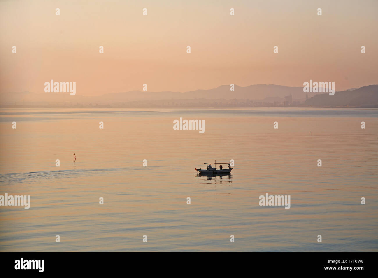 Pescatore sulla barca controllando la sua cattura a sunrise in Beppu Giappone Foto Stock