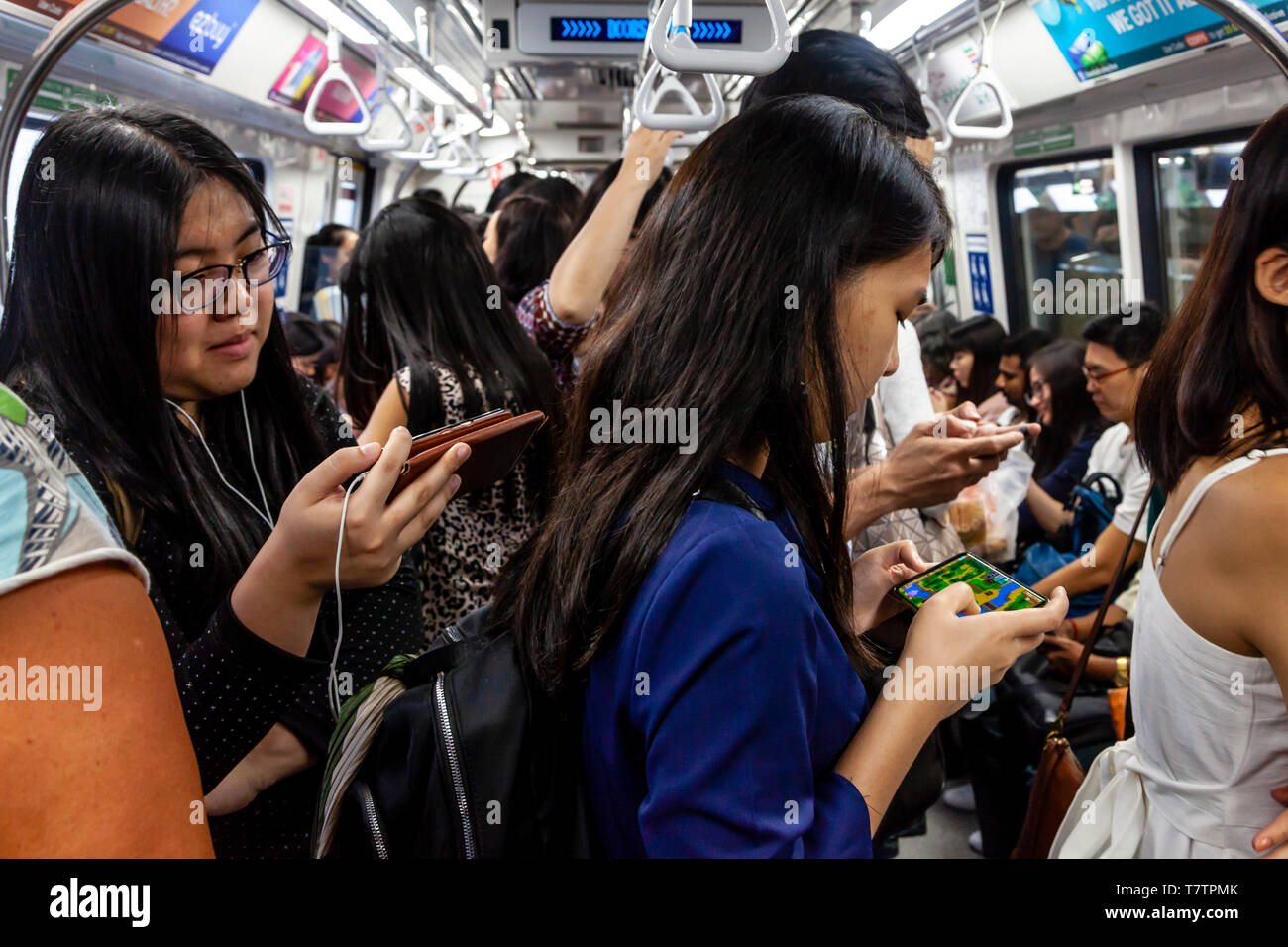 Giovani guardando i loro smartphone su MRT, Singapore, Sud-est asiatico Foto Stock
