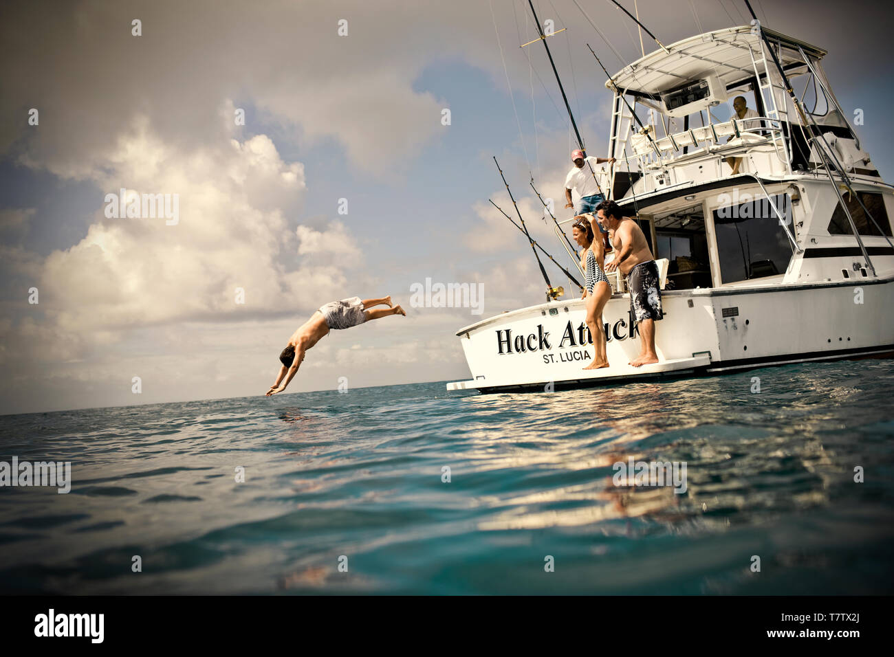 L'uomo le immersioni fuori dalla parte laterale di una barca mentre viene guardato da amici. Foto Stock