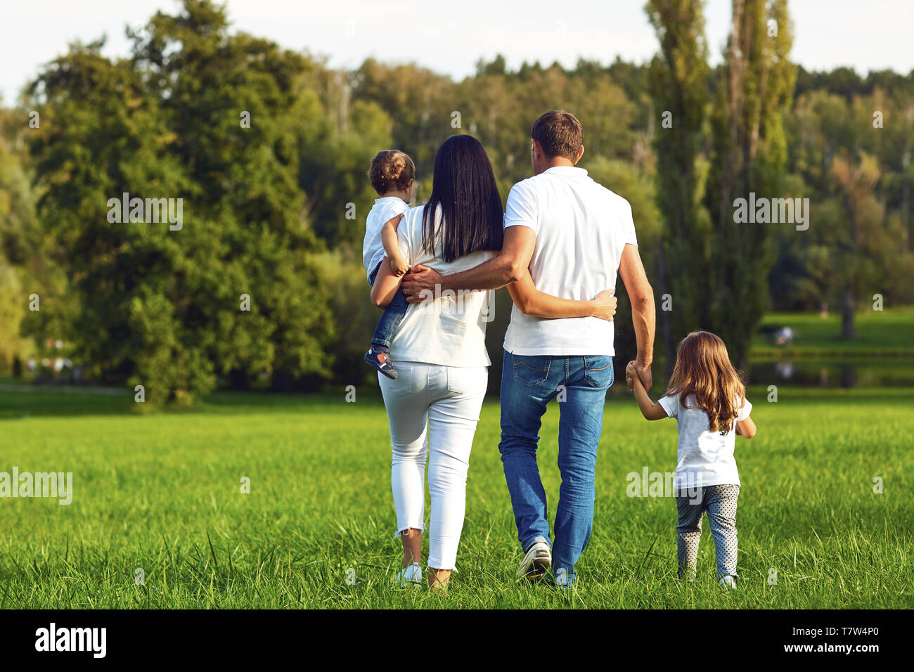 Vista posteriore. La famiglia felice con bambini passeggiate nel parco. Foto Stock