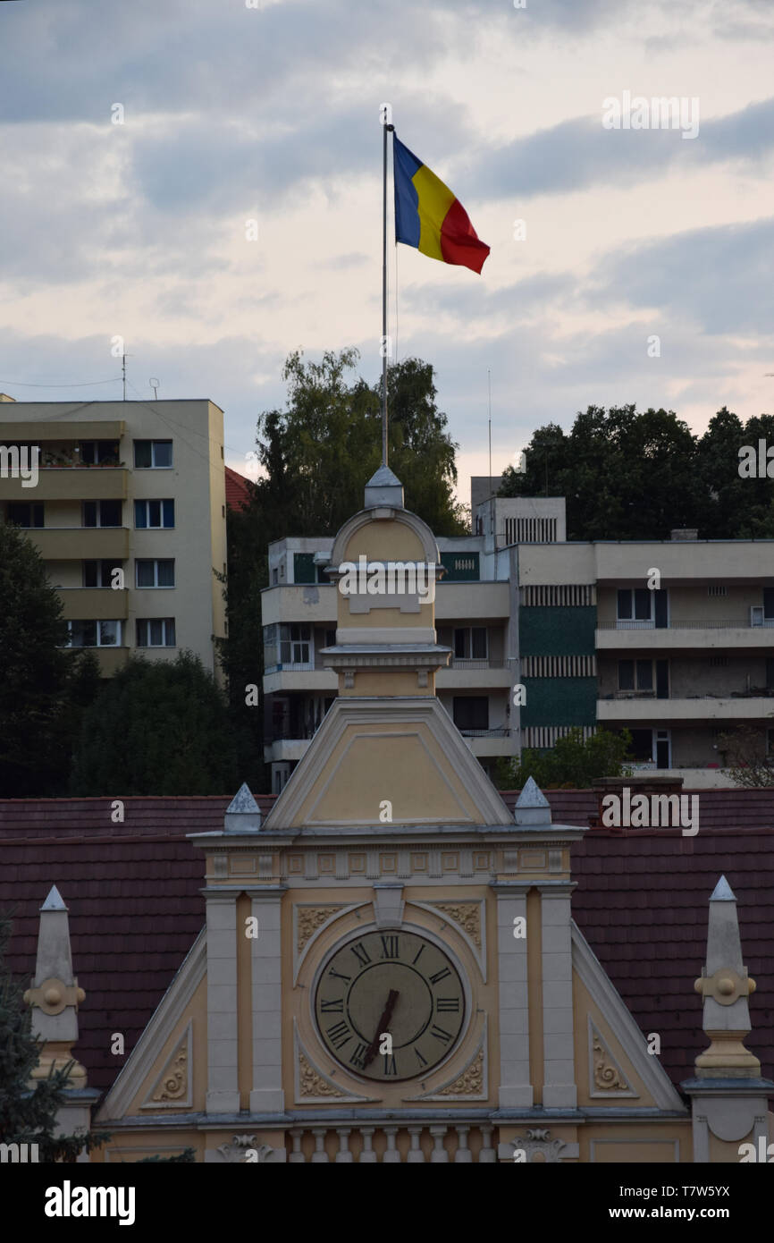 Brasov, Romania - Agosto 2017: Bandiera della Romania e orologio sulla Città di Brasov facciata Hall (Primaria Municipiului Brasov). Transilvania, Romania. Foto Stock