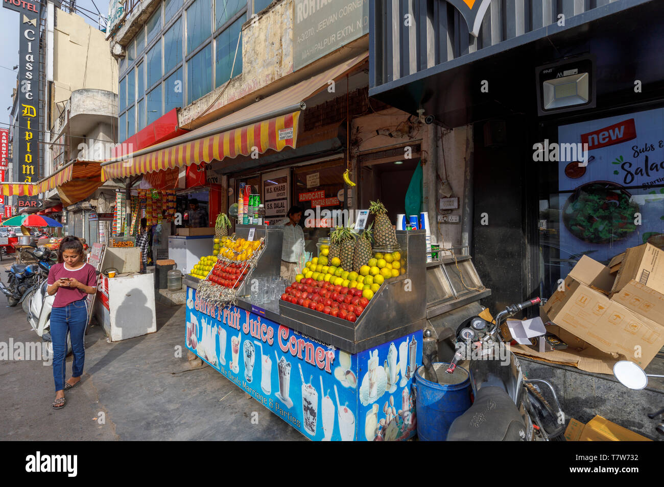 Scena di strada nel quartiere Mahipalpur, un sobborgo vicino all'Aeroporto di Delhi a Nuova Delhi, capitale dell India: ragazza locale da una frutta e succo di stallo stradale Foto Stock