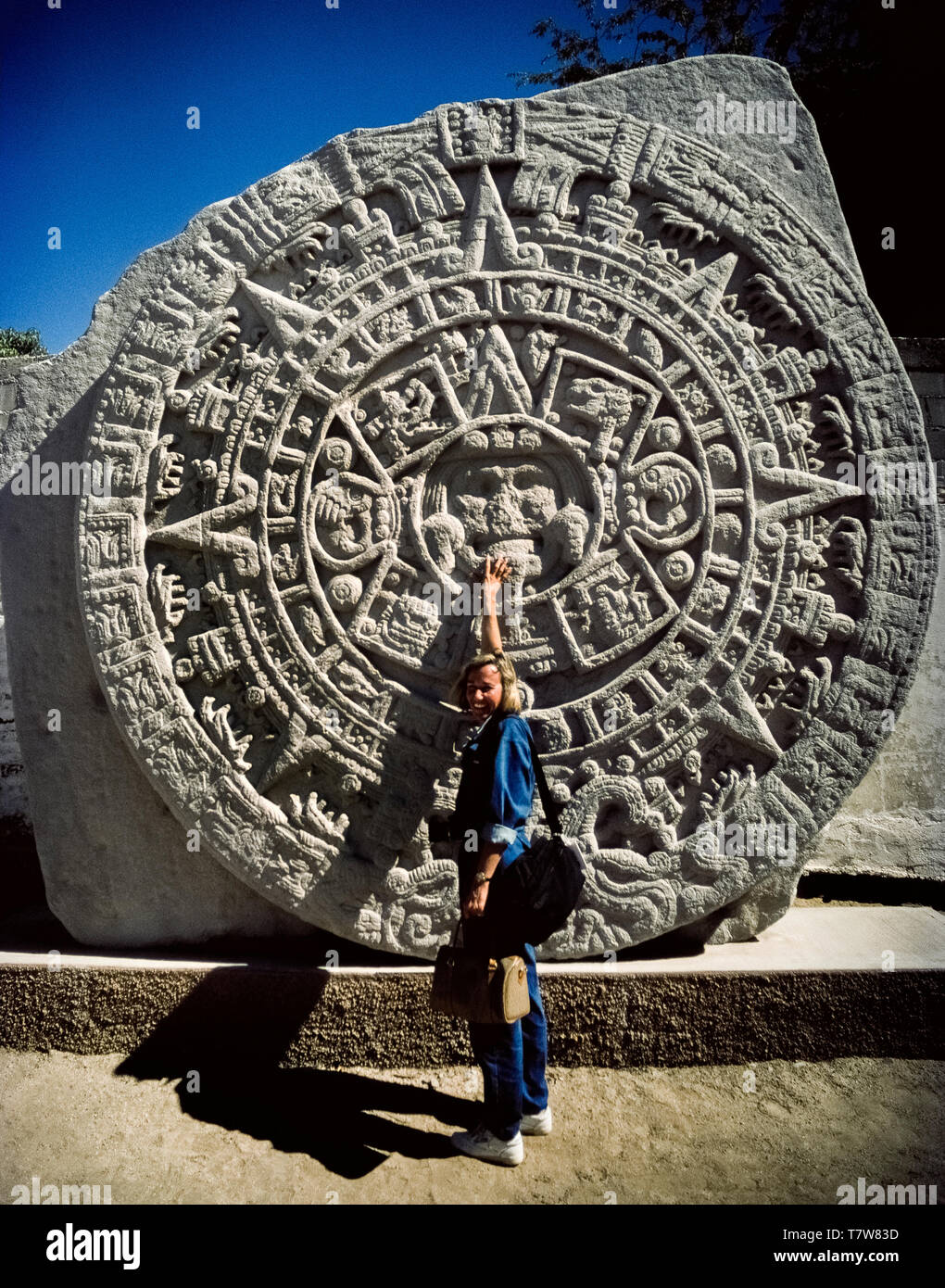 Una donna i punti turistici alla faccia del sole azteca dio che è il centro di questa replica di un messicano importante scoperta archeologica di una massiccia carving noto come il Calendario azteco pietra sul display in La Paz, la capitale della Baja California Sur in Messico, America del Nord. Chiamato anche l'Aztec pietra del sole, il basalto originale disco era trovato a Città del Messico nel 1790. I geroglifici sul monolito circolare riguardano la mitologia di ri-creazione del mondo Aztecan nel XVI secolo. Foto Stock