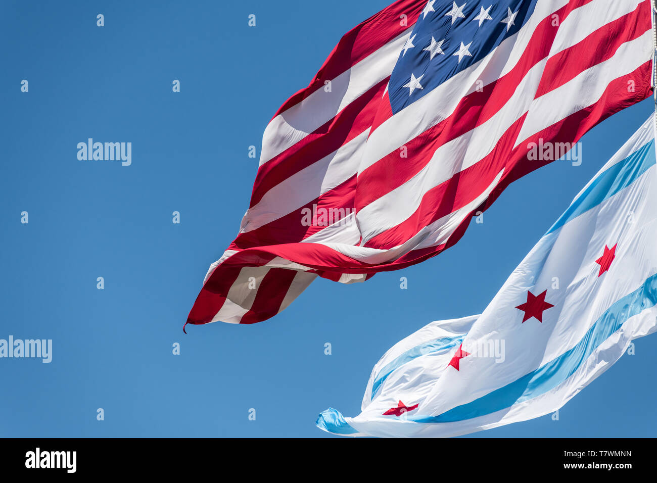 La bandiera comunale di Chicago e la bandiera americana al vento a Chicago contro il cielo blu chiaro Foto Stock