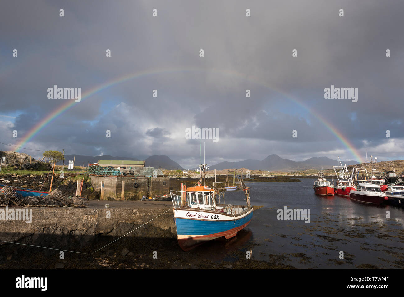 L'Irlanda, nella contea di Galway, Ballynakill, Connemara, barche in legno e barche da pesca nel porto, Tully montagne e dodici Bens montagne sullo sfondo Foto Stock
