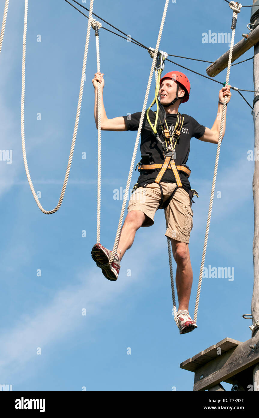 Giovane uomo ha divertimento mentre sollevando un esercizio di equilibrio in corde alte park Foto Stock