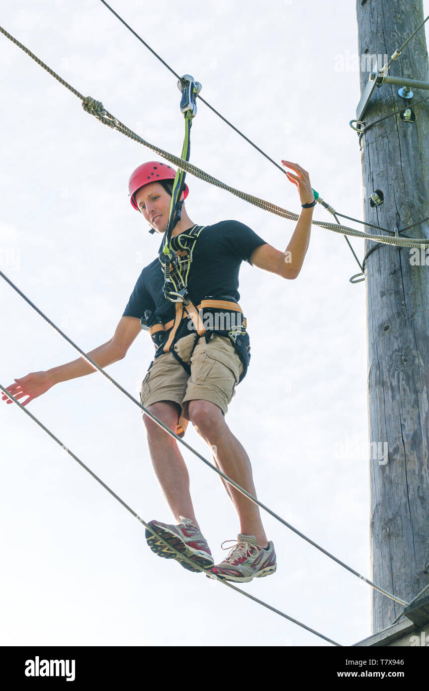 Giovane uomo ha divertimento mentre sollevando un esercizio di equilibrio in corde alte park Foto Stock