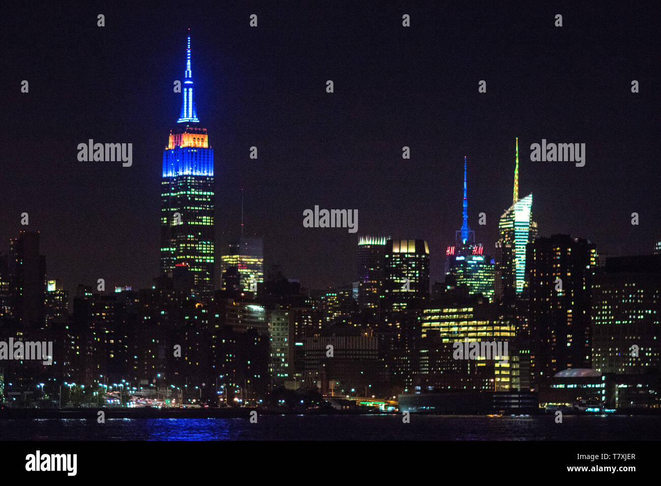 Notturna dello Skyline di Manhattan, con l'Empire State Building, ESB, illuminato in blu e arancione in onore del New York isolani. Foto Stock
