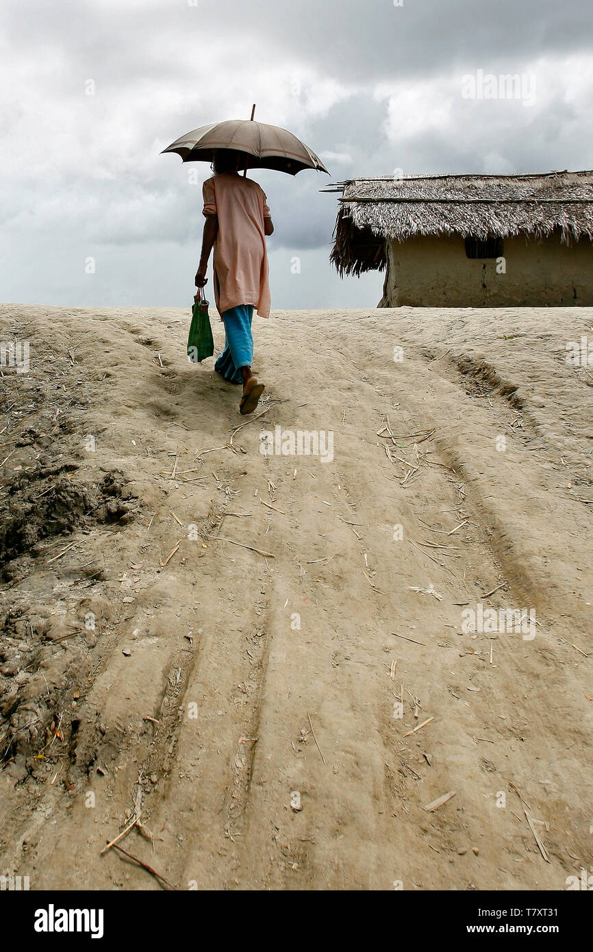 Un uomo con un ombrello passeggiate su di una ripida bordo di un argine flood costruito per schermare il Burigoalini contro le inondazioni e l'Onda di tempesta. Il Bangladesh è soggetto a un doppio smacco di inondazioni e siccità causata dalla fusione dei ghiacciai del Himalaya. Foto Stock