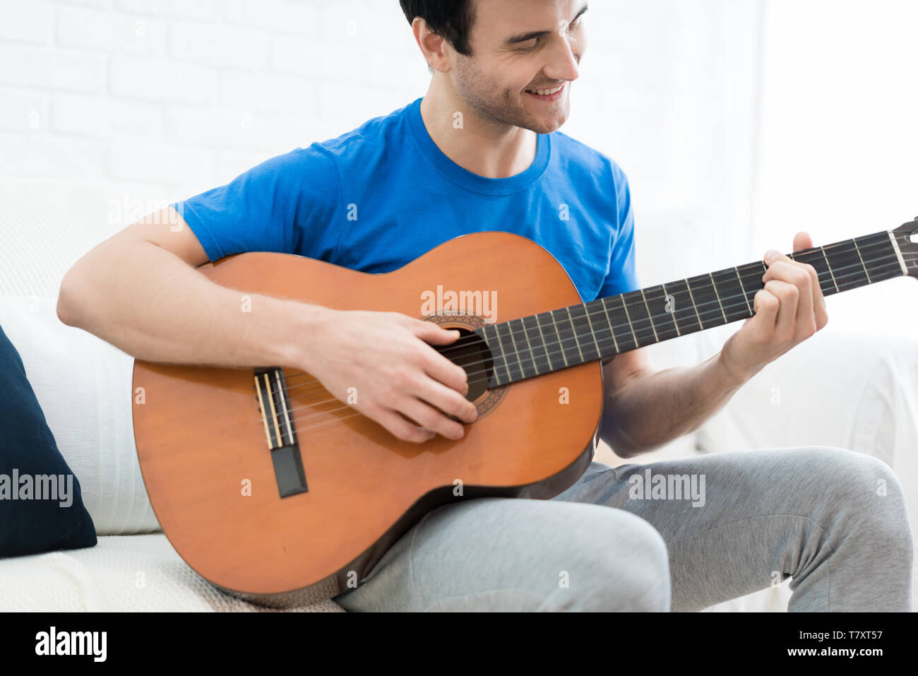 Uomo bello giocare sulla chitarra sul divano di casa. Rilassati guardando uomo seduto su un divano e suonare la chitarra. Foto Stock