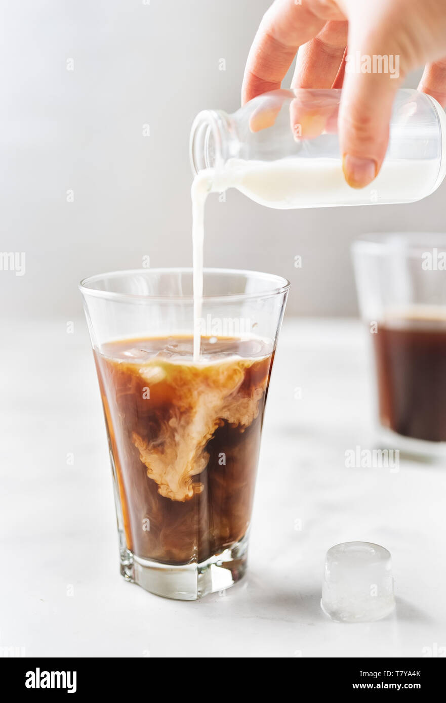 Caffè ghiacciato con colata di latte in vetro su un bianco sullo sfondo di legno Foto Stock