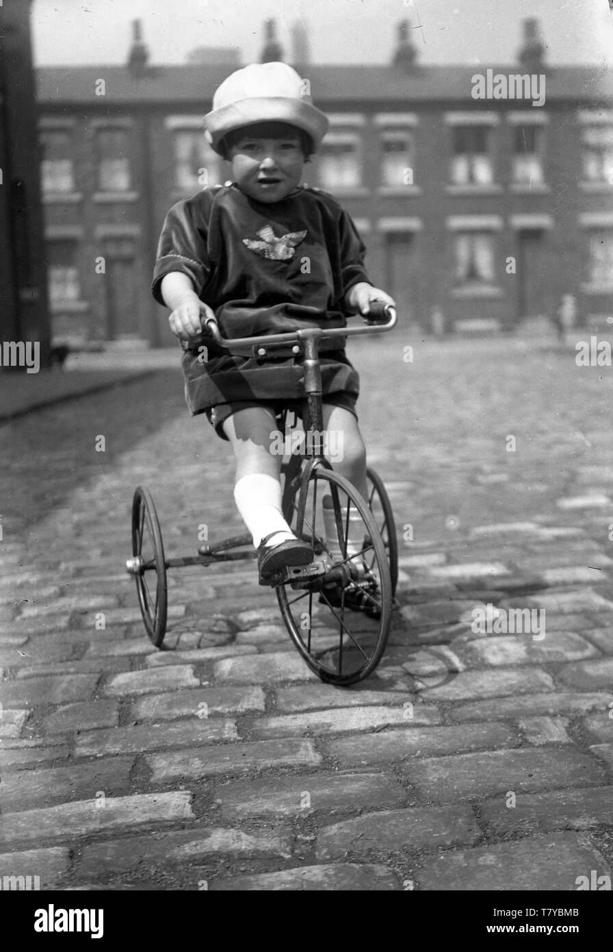 Bambino sul triciclo sulla strada di ciottoli in Gran Bretagna 1921 Foto Stock
