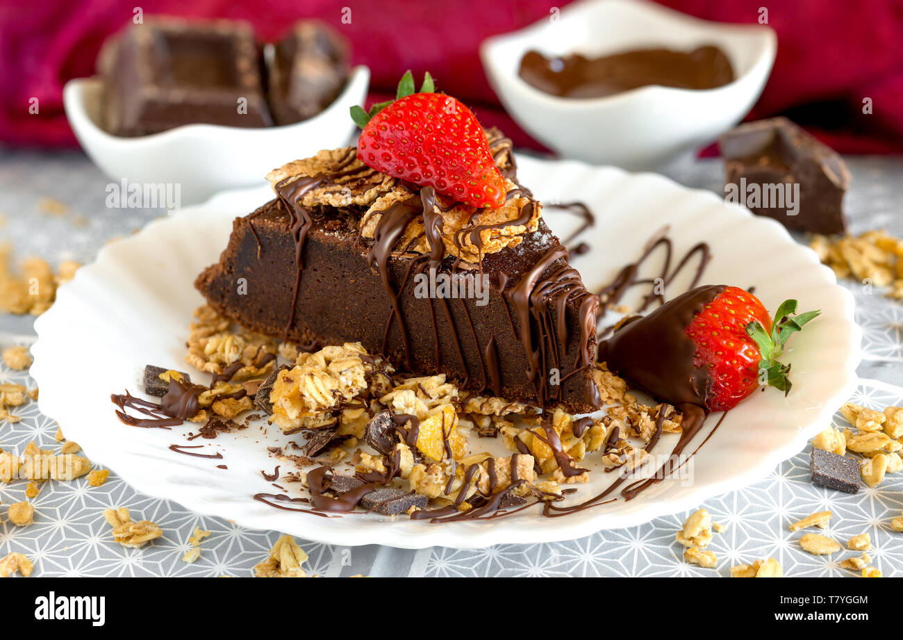Fetta di torta al cioccolato con muesli, cereali e fragole ricoperte di cioccolato fondente strisce Foto Stock