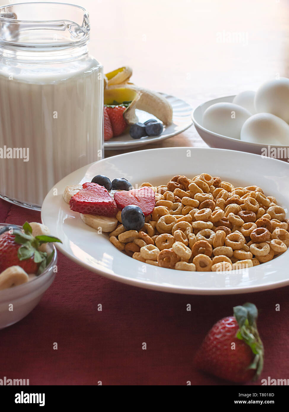 Una ciotola di cereali con frutta assortiti, latte e uova, come parte di una colazione bilanciata. Ciotola su un posto rosso opaco con tavolo in legno sfocato nella backg Foto Stock