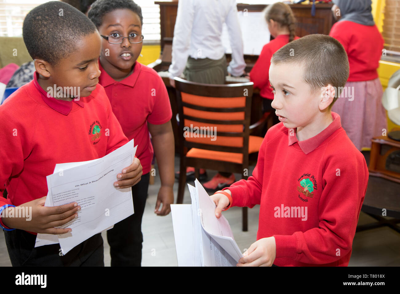 La scuola dei bambini tenendo i fogli di carta con le parole della canzone preparare a cantare con un pianoforte in sottofondo Foto Stock