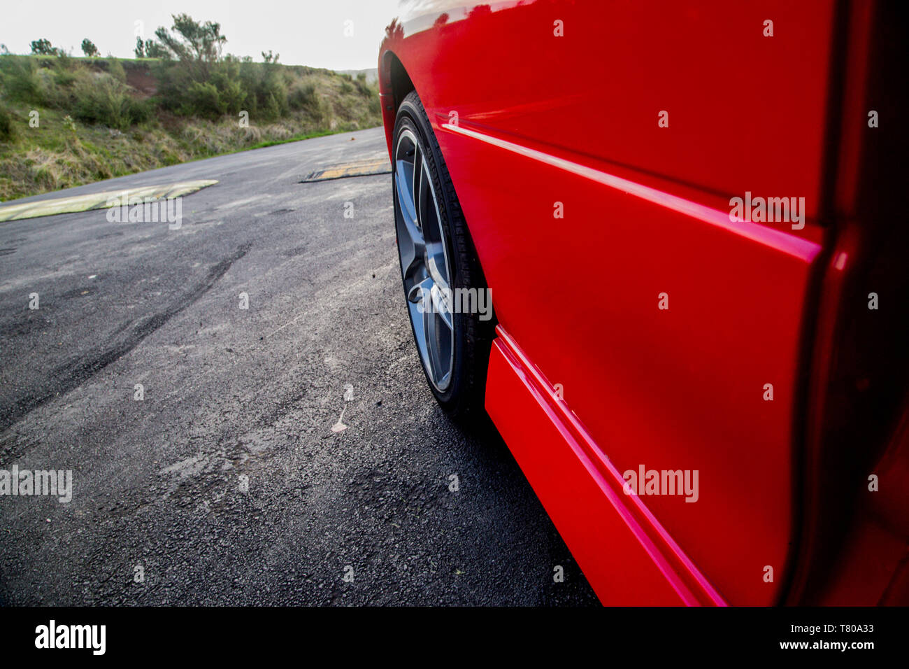 Pedane o predellini e ruota da un rosso lucido auto sportiva con un motore V8. In contrasto con il nero di asfalto e di erba in background. Foto Stock
