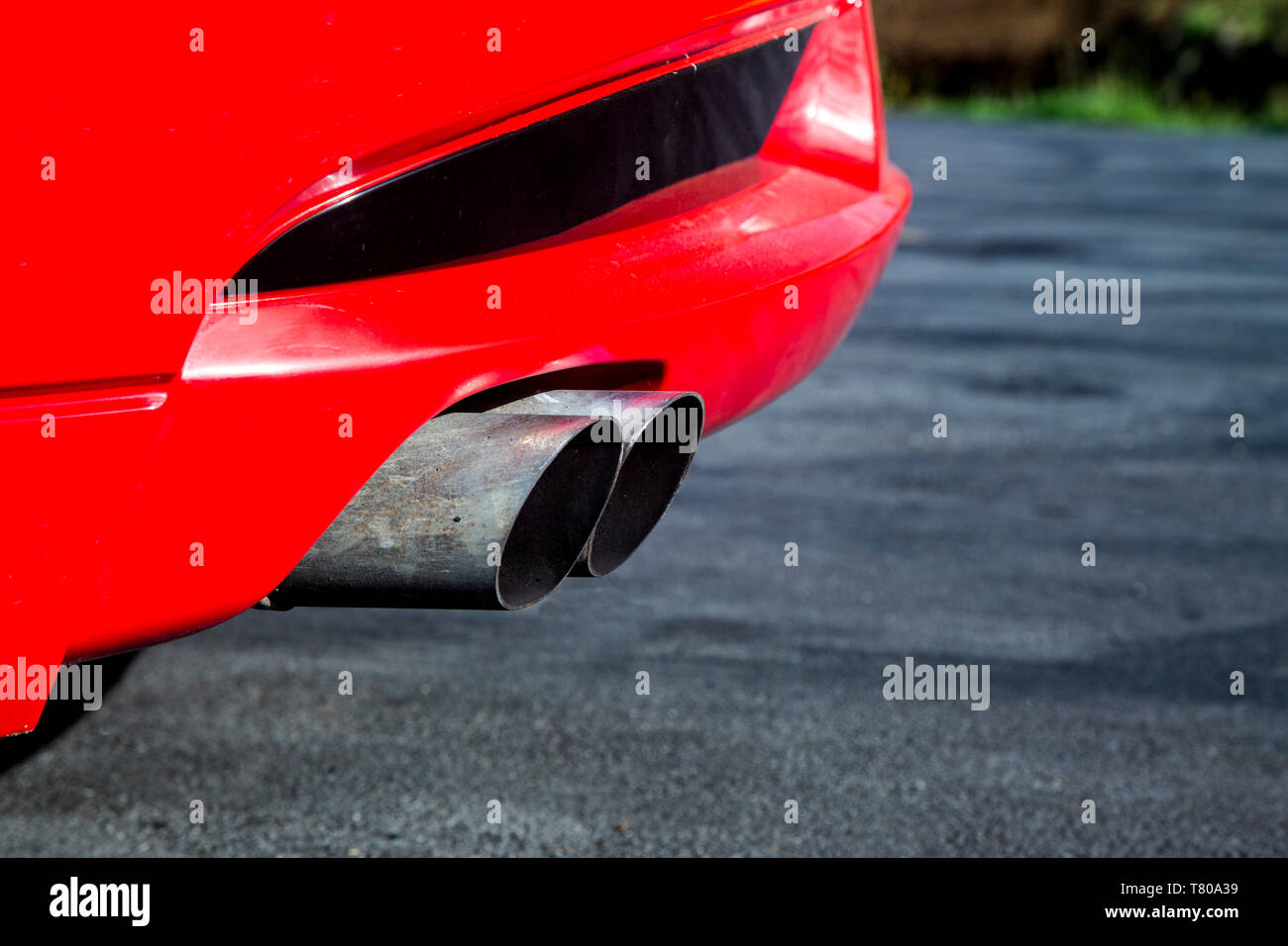 Tubi di scarico da un rosso lucido auto sportiva con un motore V8. In contrasto con il nero di asfalto e di erba in background. Foto Stock