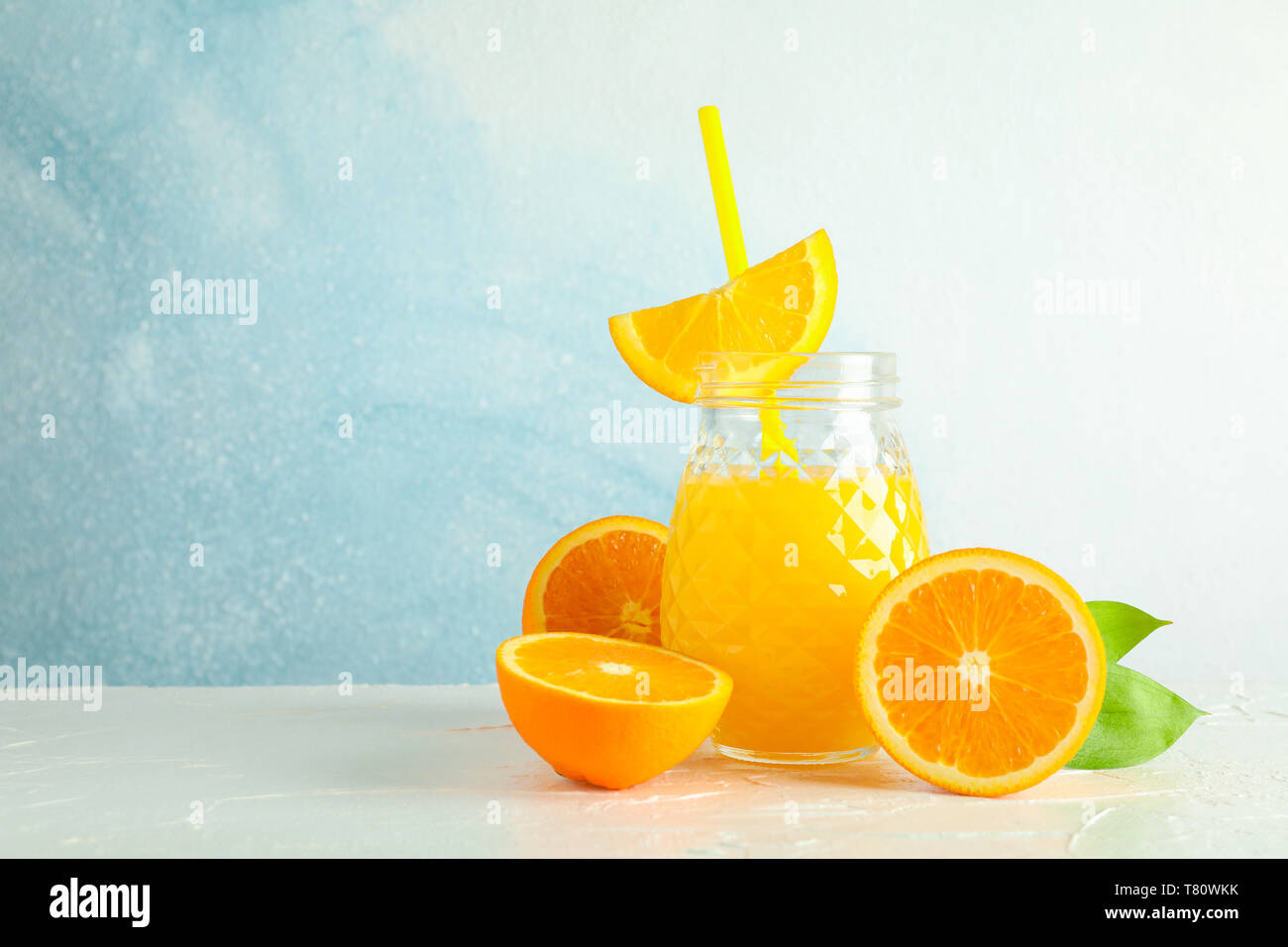 Vaso di vetro con succo d'arancia fresco e il tubicino, arance sul tavolo bianco contro il colore di sfondo, spazio per il testo. Fresca bevanda naturale Foto Stock