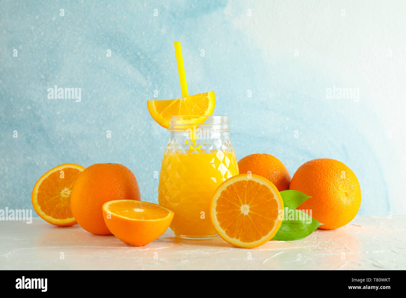 Vaso di vetro con succo d'arancia fresco e il tubicino, arance sul tavolo bianco contro il colore di sfondo, spazio per il testo. Fresca bevanda naturale Foto Stock