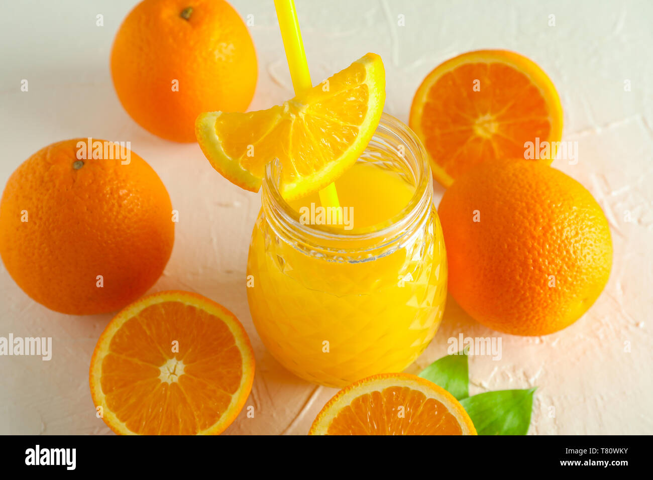Vaso di vetro con succo d'arancia fresco e il tubicino, arance, su sfondo bianco closeup. Fresca bevanda naturale Foto Stock