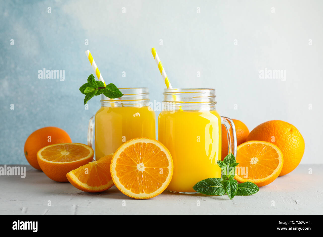 Vasi di vetro con succo d'arancia fresco e il tubicino, arance e menta sul tavolo bianco contro il colore di sfondo, spazio per il testo. Fresca bevanda naturale Foto Stock
