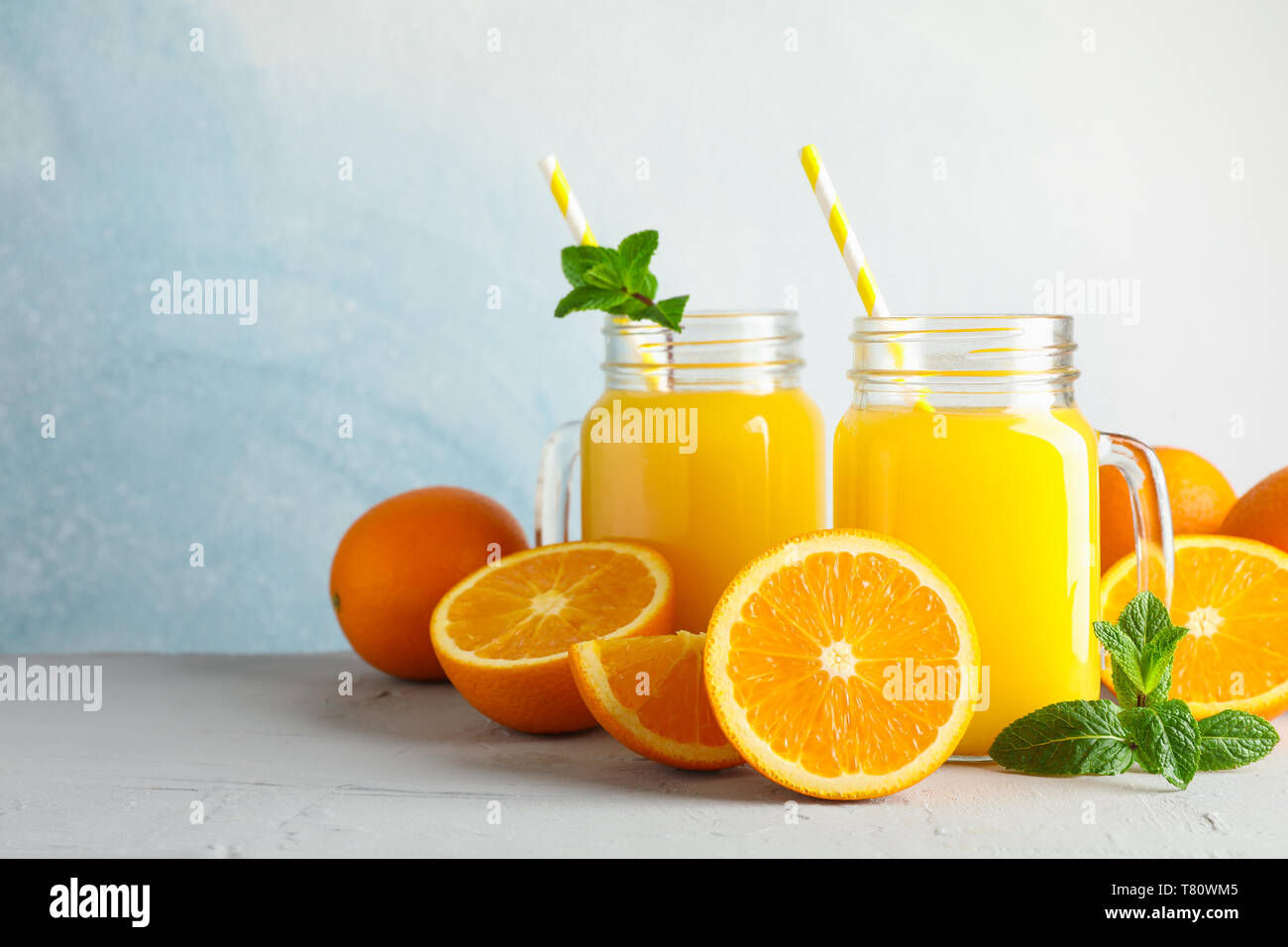 Vasi di vetro con succo d'arancia fresco e il tubicino, arance e menta sul tavolo bianco contro il colore di sfondo, spazio per il testo. Fresca bevanda naturale Foto Stock