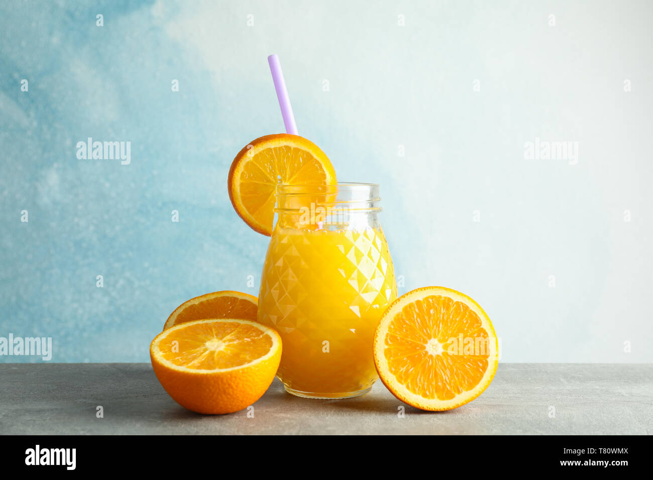 Vaso di vetro con succo d'arancia fresco, tubicino e arance sulla tabella grigia contro il colore di sfondo, spazio per il testo. Fresca bevanda naturale Foto Stock