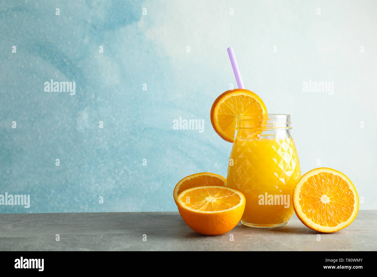 Vaso di vetro con succo d'arancia fresco, tubicino e arance sulla tabella grigia contro il colore di sfondo, spazio per il testo. Fresca bevanda naturale Foto Stock