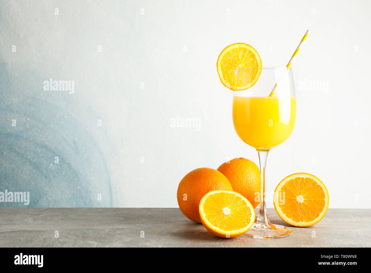Vetro con succo d'arancia fresco e il tubicino, arance sulla tabella grigia contro il colore di sfondo, spazio per il testo. Fresca bevanda naturale Foto Stock