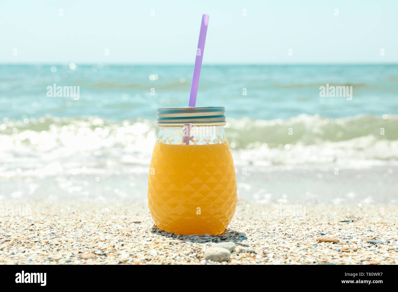 Il vasetto di vetro di succo d'arancia fresco sul mare, lo spazio per il testo. La vacanza estiva lo sfondo Foto Stock