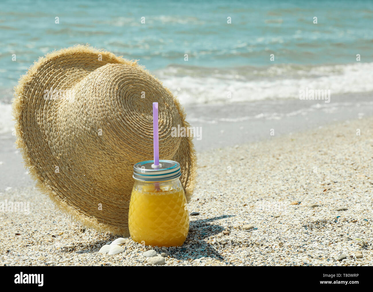 Cappello di paglia e succo di arancia sul mare, lo spazio per il testo. La vacanza estiva lo sfondo Foto Stock