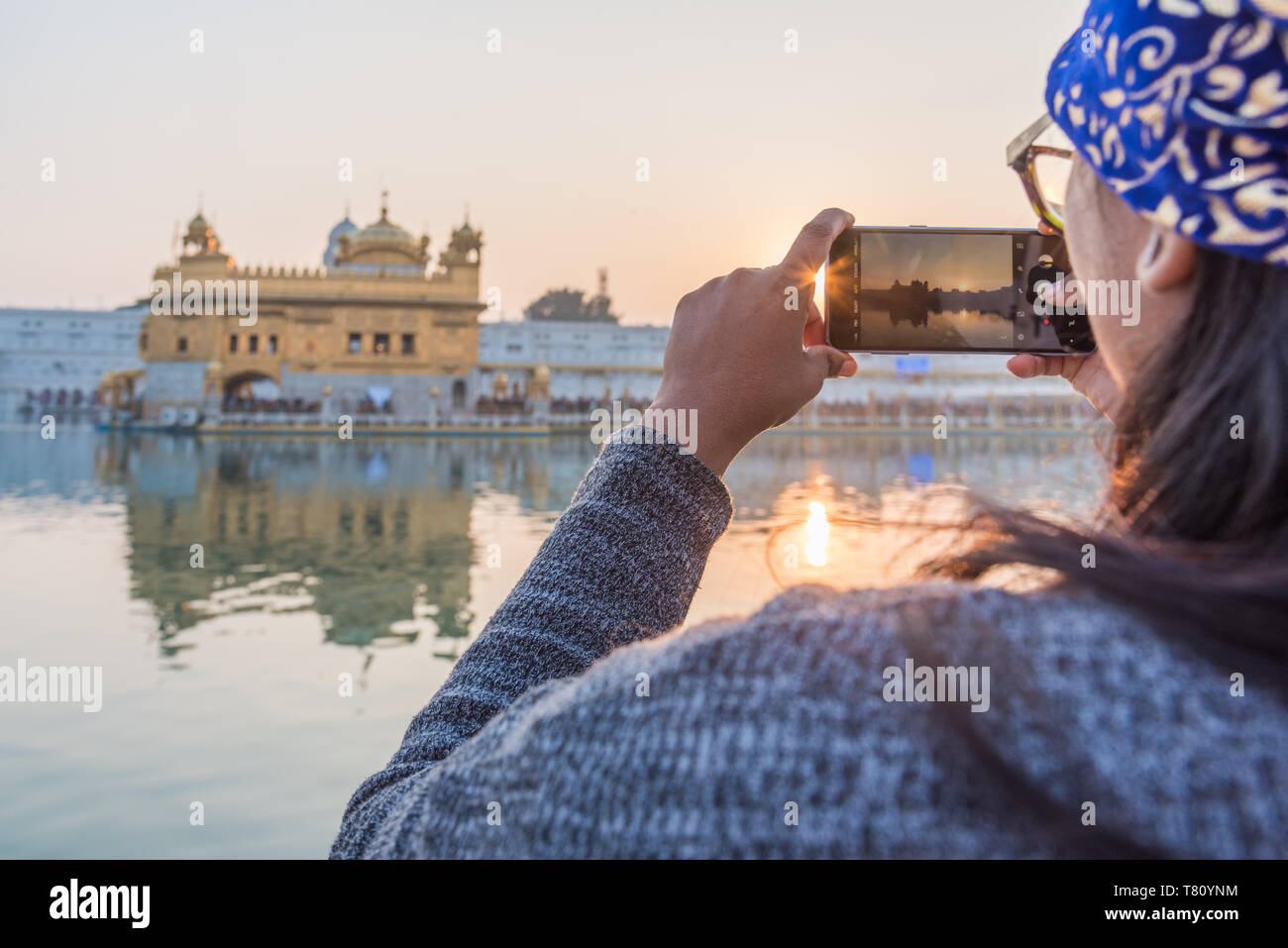 Una signora indiana prende uno smartphone foto del tempio d'Oro al tramonto il Tempio Dorato, Amritsar Punjab, India, Asia Foto Stock