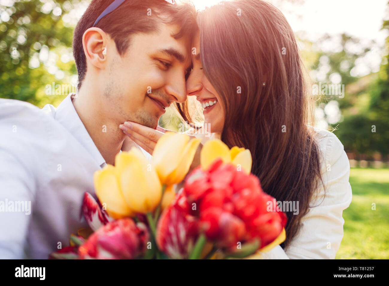 Felice coppia giovane in amore abbracciando con molla bouquet di fiori all'esterno. L'uomo dotato della sua fidanzata con i tulipani Foto Stock