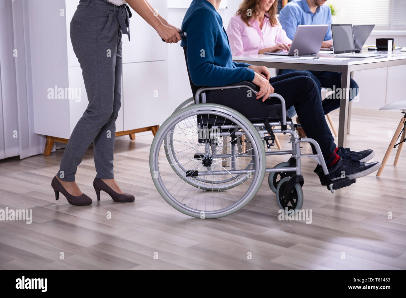 Sorridente giovane imprenditrice aiutando collega disabili in sedia a rotelle Foto Stock