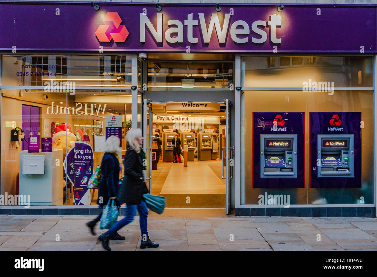 Un Natwest Bank Building a Oxford, UK, con due donne passato a piedi con le borse della spesa. Dicembre 2018. Foto Stock