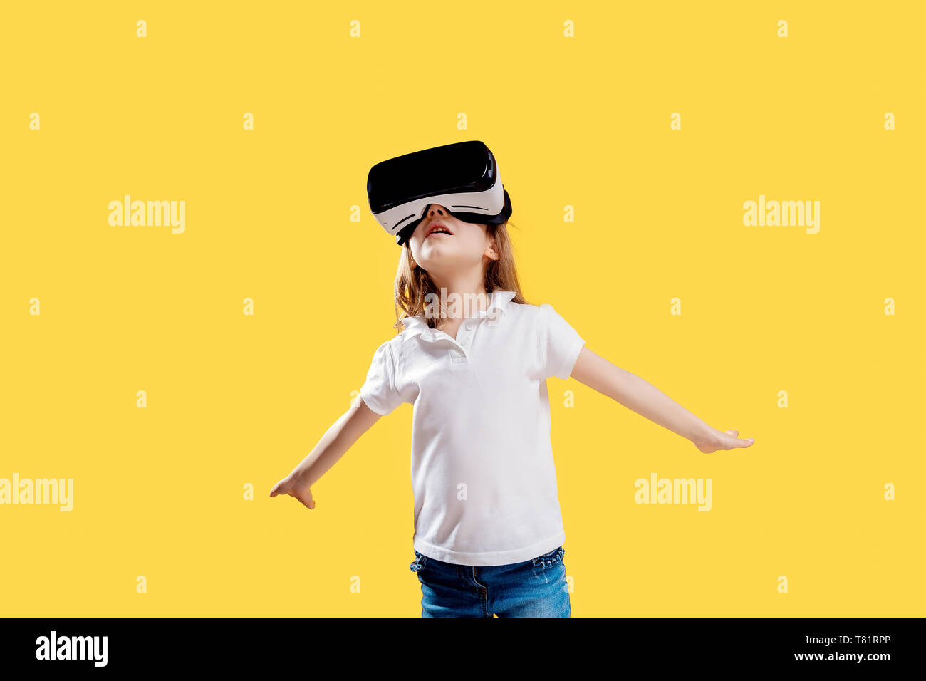 Ragazza 7 anni in abito formale che indossa gli occhiali VR mettendo le mani in emozione isolato su sfondo giallo. Bambino usando un gadget di gioco di realtà virtuale. La tecnologia virtuale. Foto Stock