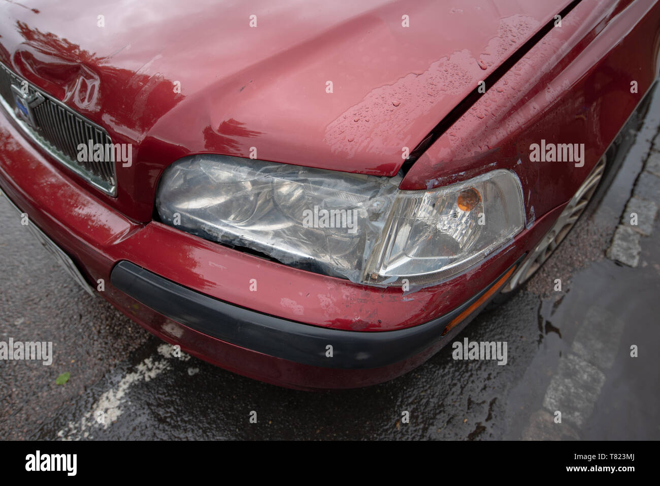 Scontro del veicolo. Rotto il faro e il paraurti danneggiato su una vecchia auto rossa. Incidente auto sfondo. Foto Stock