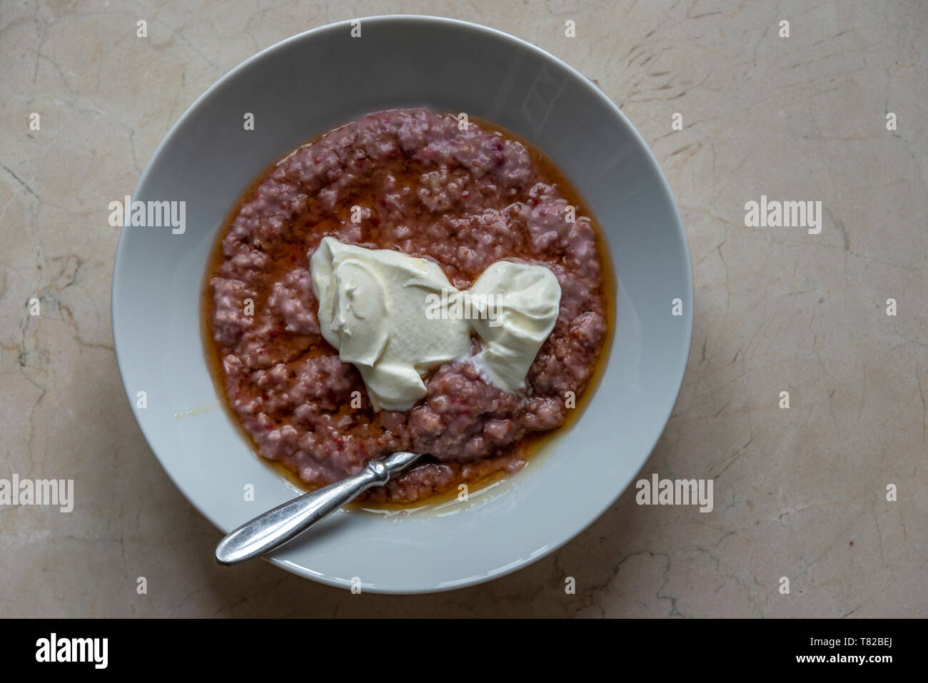 Un Birds Eye View di un piatto di polenta con cucchiaio d'argento, con yogurt naturale topping. Foto Stock