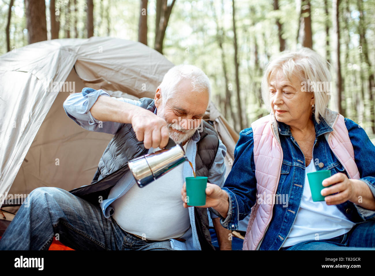 Coppia senior versando il caffè avente un picnic presso il campeggio nella foresta Foto Stock