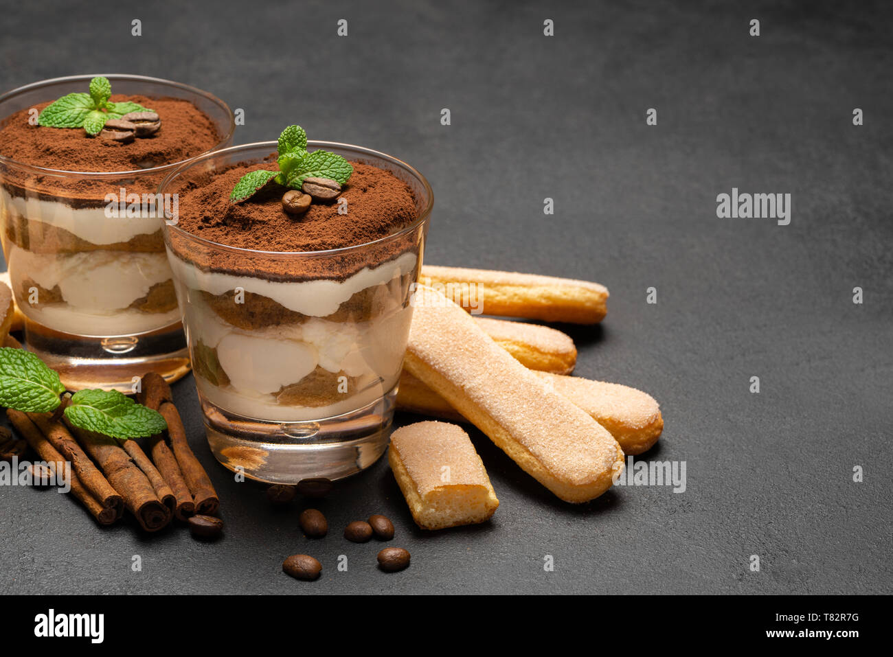 Tiramisù classico dessert in un bicchiere e savoiardi cookies sul scuro dello sfondo in calcestruzzo Foto Stock