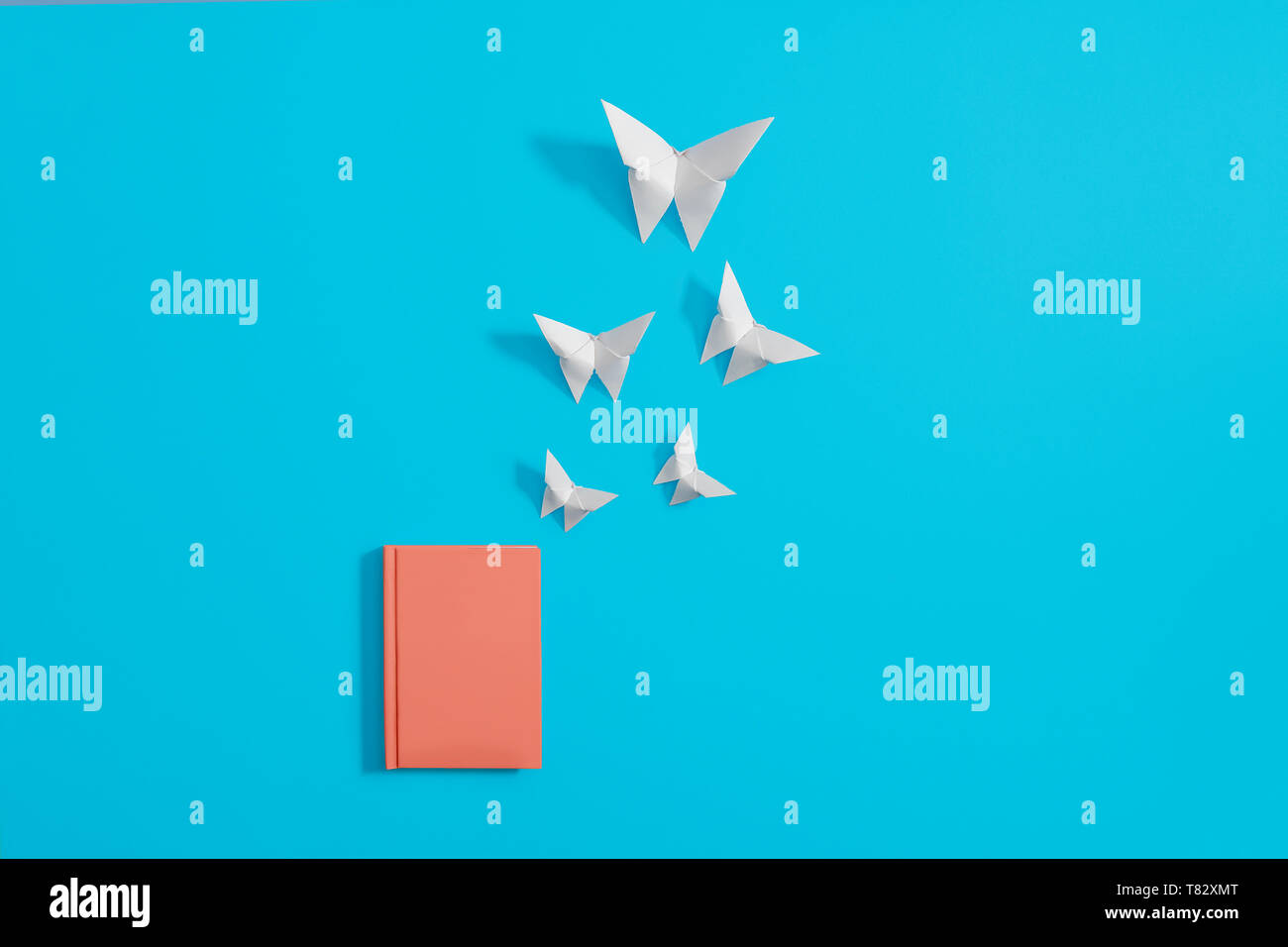 Notebook arancio, diario ufficiale su uno sfondo blu con la carta origami farfalle volare fuori di esso con copia e spazio per il testo Foto Stock