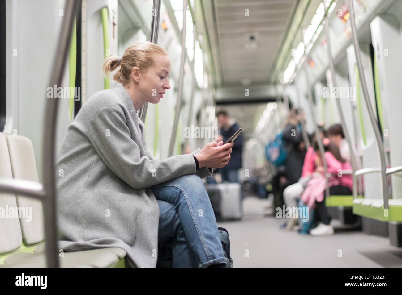 Bella donna bionda che indossa cappotto invernale la lettura al telefono mentre si è in viaggio in metropolitana dei trasporti pubblici. Foto Stock